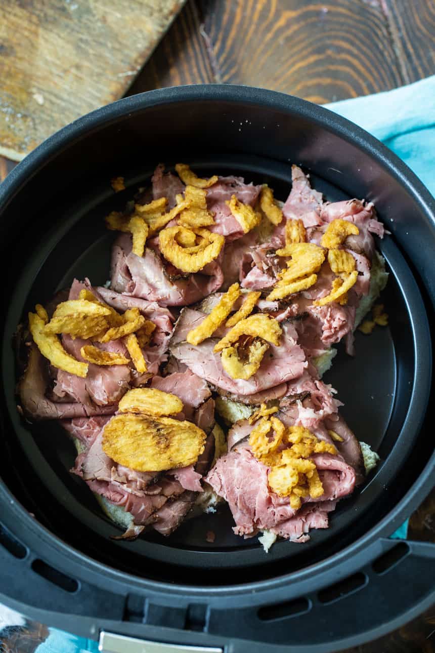Hawaiian Rolls topped with roast beef and onions in air fryer basket.