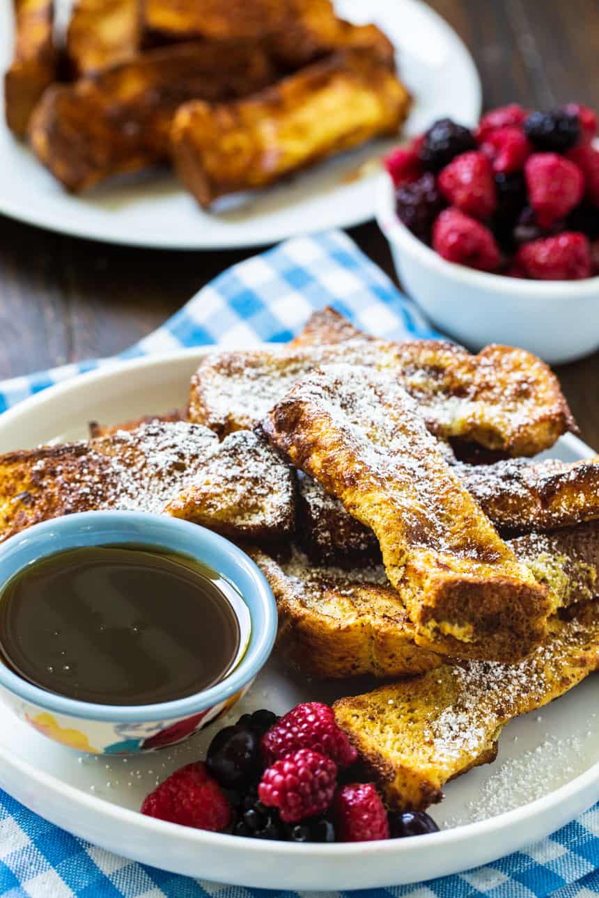 French Toast sticks on a plate with maple syrup and berries.