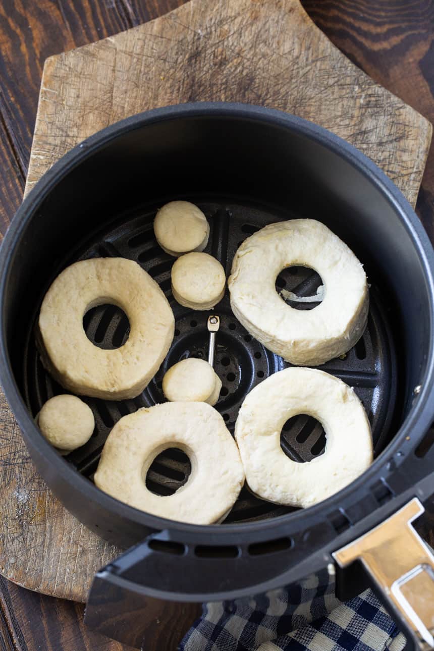 Uncooked doughnuts in air fryer basket.