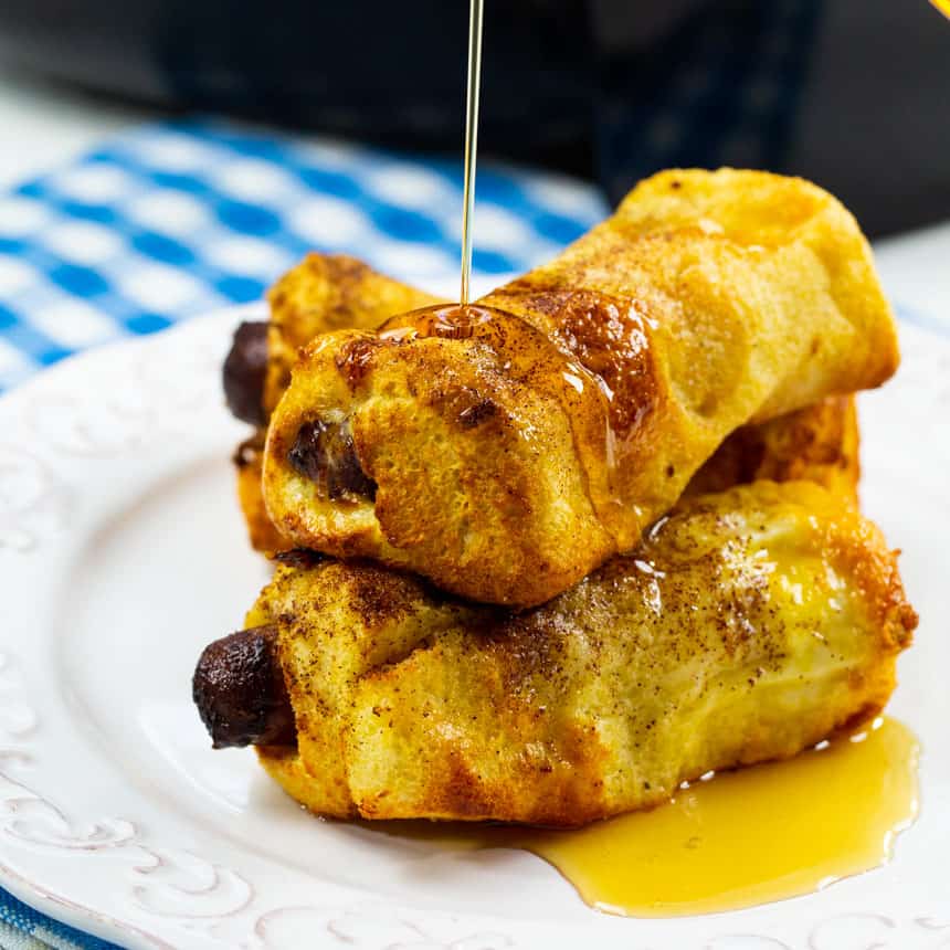 Three French Toast Roll-Ups on a plate getting drizzled with syrup.