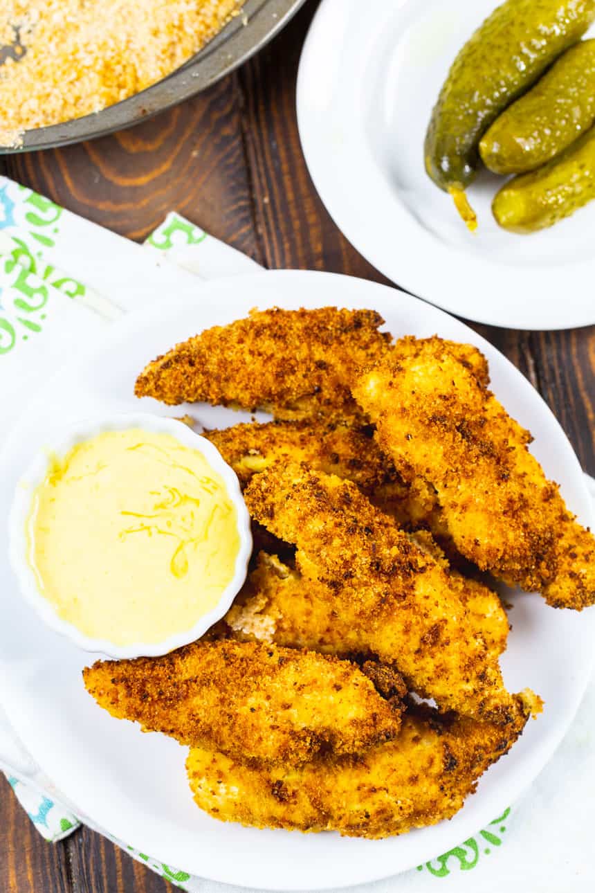 Plate of chicken tenders next to a plate of pickles.