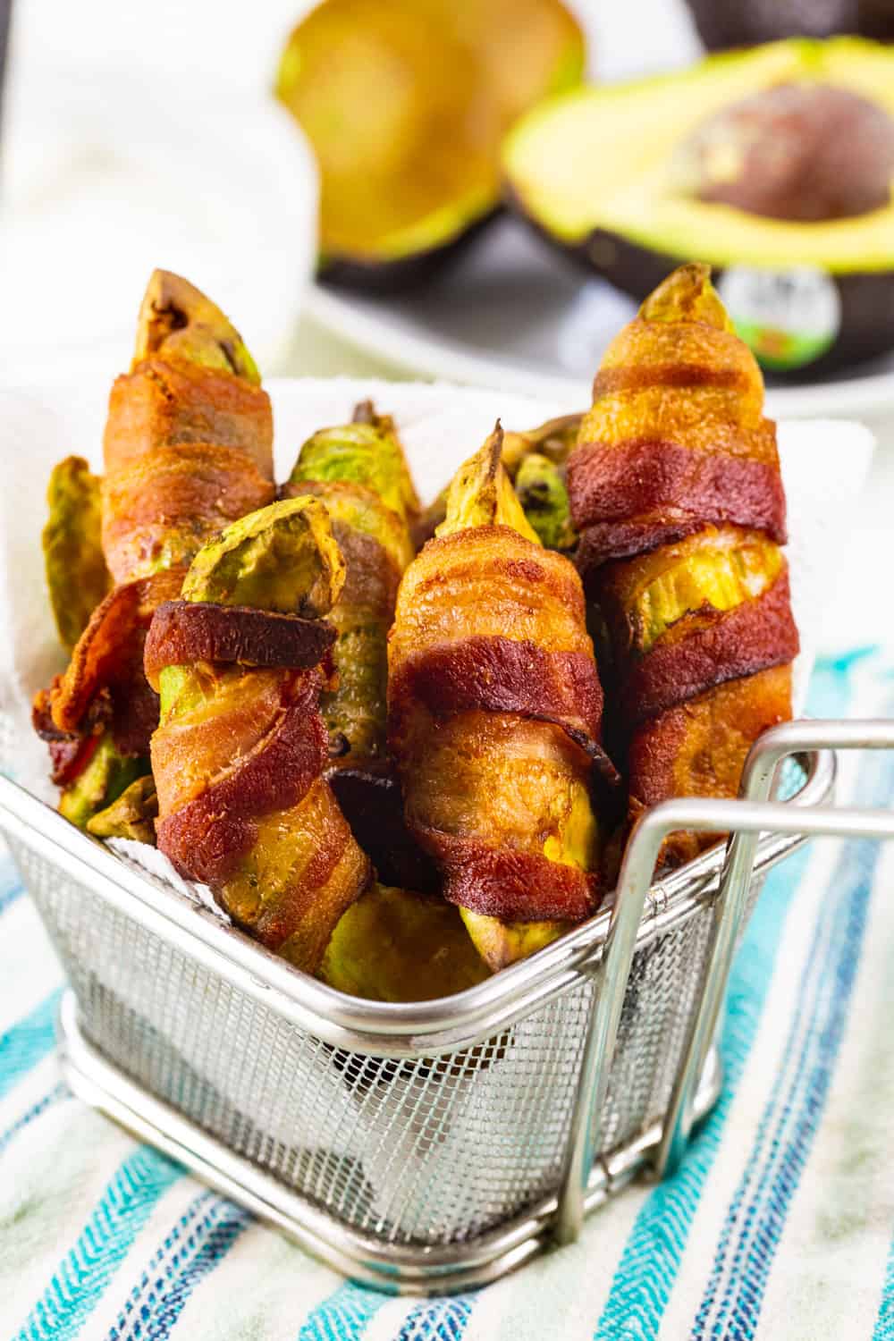 Air Fryer Bacon Wrapped Avocado Fries in small metal basket.