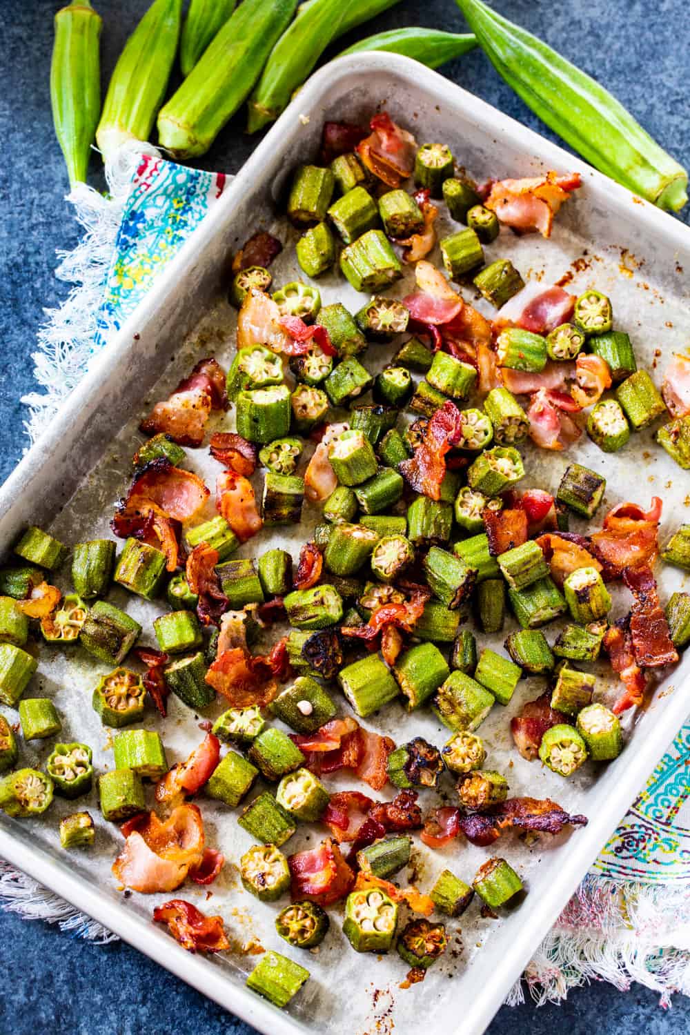 Okra and Bacon on rimmed baking sheet with fresh okra next to it.