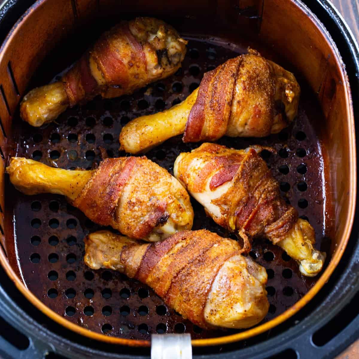 Bacon-wrapped Chicken Legs in air fryer basket.